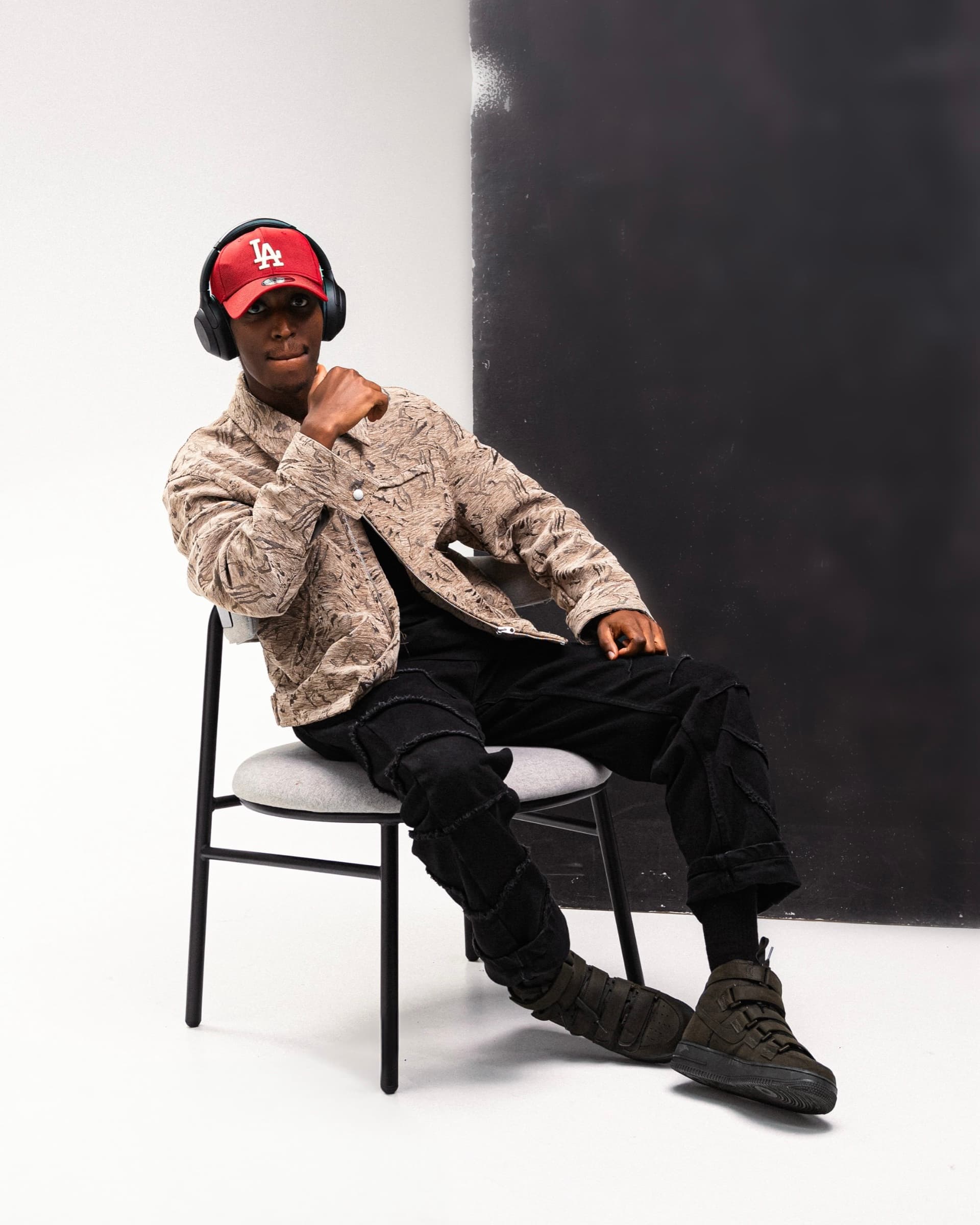 Editorial studio portrait of Aminu Hassan Iradukunda (Creative Aminu) seated, wearing a red cap and headphones